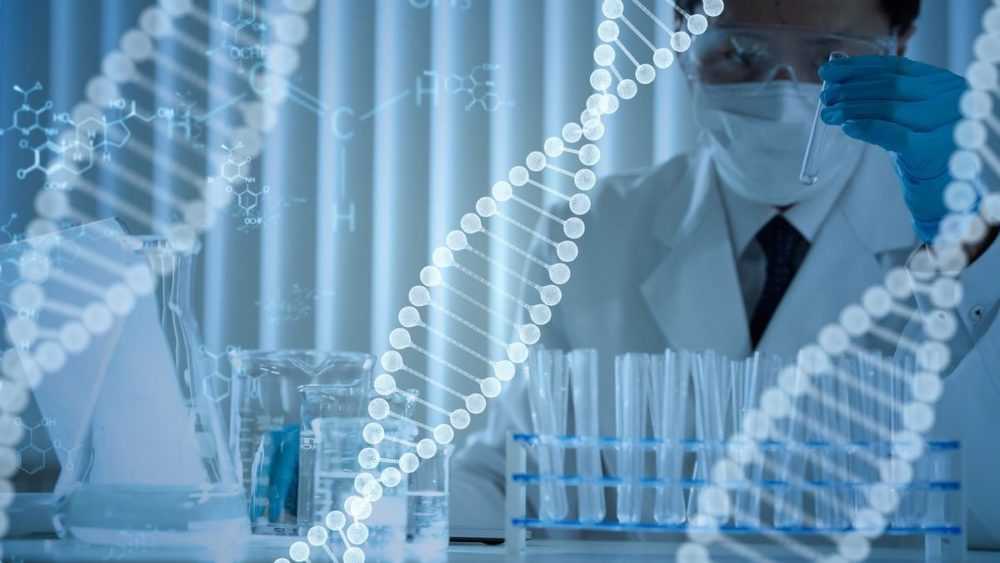 A man looks at a glass test tube in a lab, with beakers and additional tubes on a surface in front of him. Overlaid on the image are strands of double-helix DNA and chemistry diagrams.