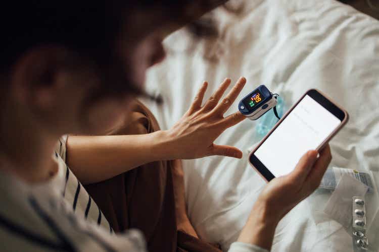A From Above Shot Of An Unrecognizable Woman Measuring The Oxygen Saturation Level Of Her Blood After Recovering From Coronavirus While Watching Something On Her Smartphone