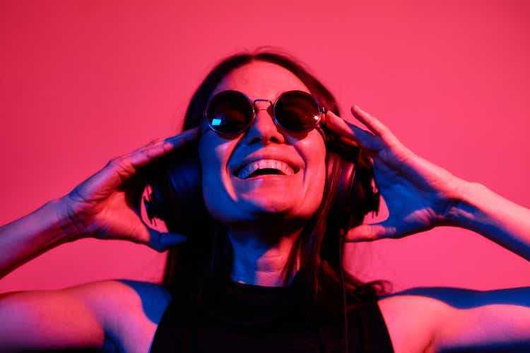 Pretty woman with sunglasses listening to music with headphones on neon background