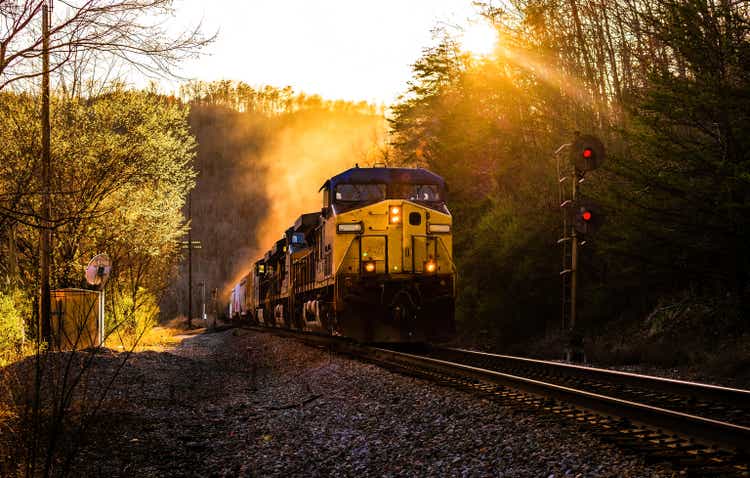 A cargo locomotive engine train is in the valley and sun is going to rise in the morning for local transportation.