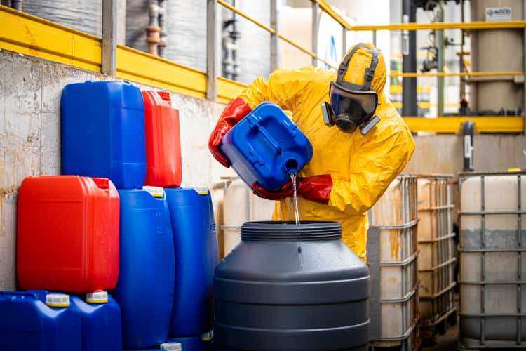 Химик или технолог в желтом защитном костюме и противогазе, производящий серную кислоту для промышленности.
