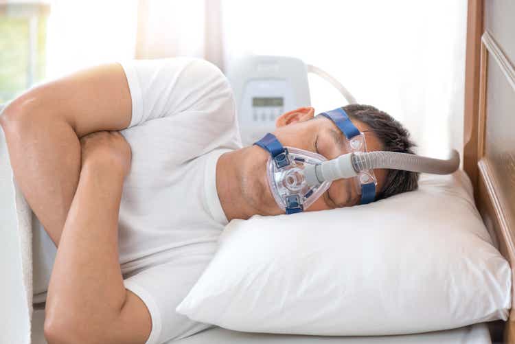 Мужчина спит в постели в маске CPAP, терапия апноэ во сне
