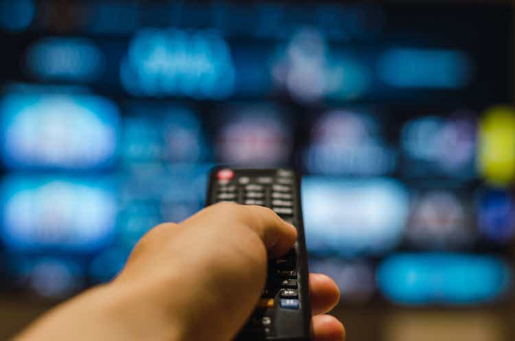Cropped hand of man holding remote control and watching smart tv in living room