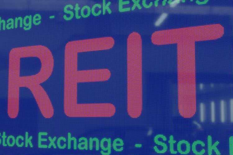 REIT (инвестиционные фонды недвижимости) на синем светодиодном экране, обрамленном зеленым текстом фондовой биржи.