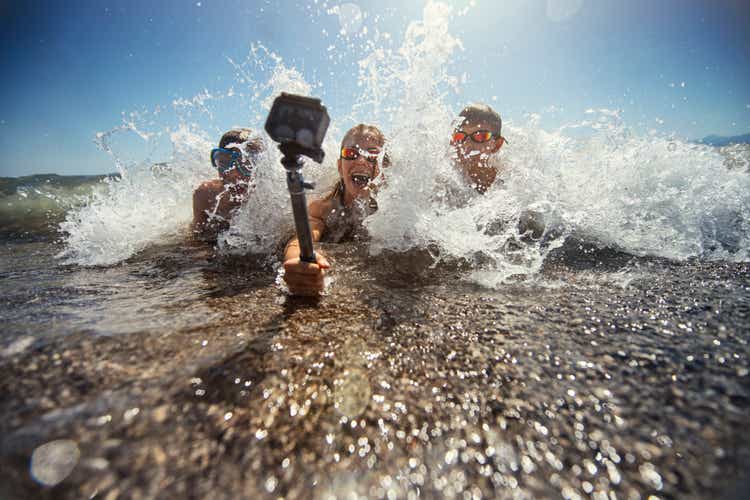 Дети играют в морских волнах и снимают себя на водонепроницаемую экшн-камеру.