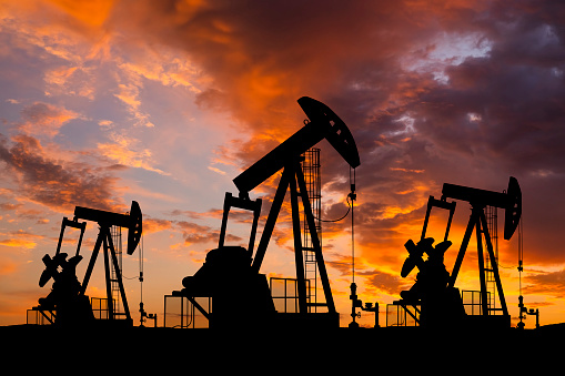 Нефтяное месторождение с буровыми установками и насосами на закате. Мировая нефтяная промышленность