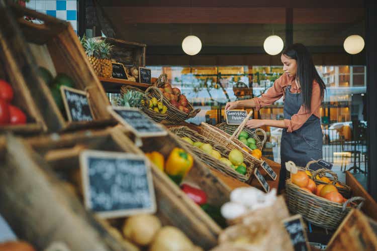 Женщина-владелица супермаркета расставляет вывески с продуктами, выставленными возле ее магазина
