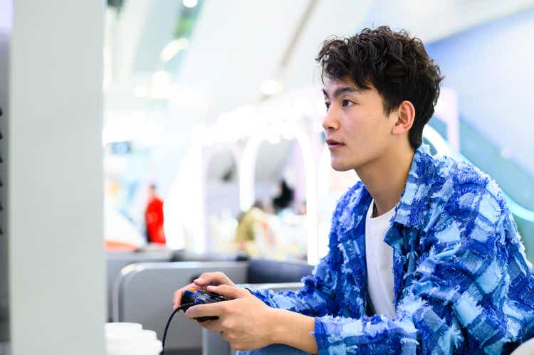 Азиатский молодой человек играет в видеоигру с игровым контроллером