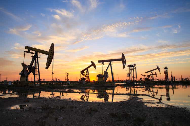 Месторождение нефти, вечером работают масляные насосы, масляный насос и красивый закат отражаются в воде